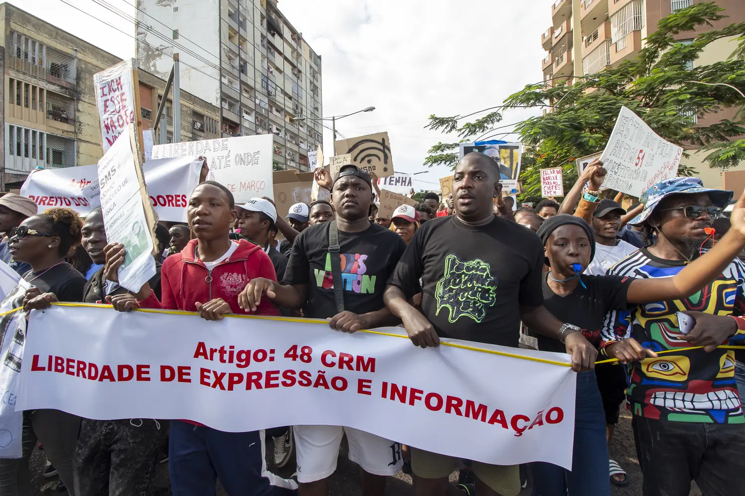 Manifestantes, incuindo Puto Aires, carregando um banner que invoga o Artigo 48 da Constituição da República que invoca a Libertdade de Expressão e Informação